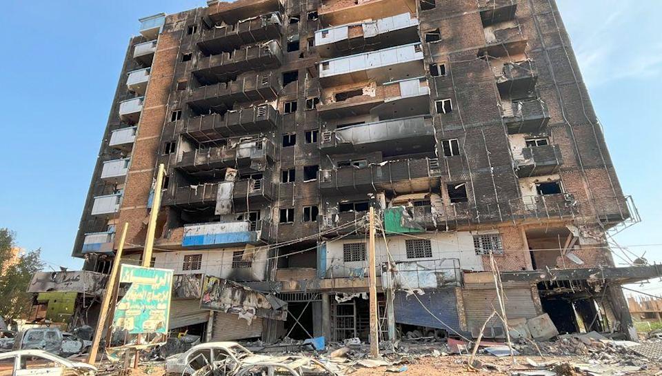 The charred carcass of a building with balconies in the Haj Yusuf district of Sudan&#39;s capital Khartoum. The wreckage of white cars can be seen in front - March 2025