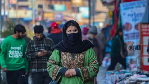 Getty Images A woman wearing a protective face mask walks along a road in Srinagar, Jammu and Kashmir, on January 15, 2025. 