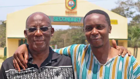 Sulley Lansah Mark Wilberforce (R) in a green, white and yellow stripped top stands outside Tema Secondary School with his Uncle Jojo