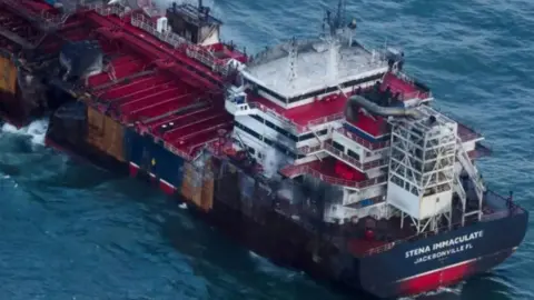 Reuters A large oil tanker with a gaping hole in its port [left] side. The area around the bridge, at the stern of the ship, is blackened from fire. 