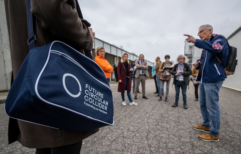 A person holds a bag with a logo of the Future Circular Collider in front of a crowd listening to CERN's Eenergy coordinator Serge Claudet (Far R).