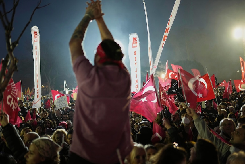 A man claps his hand in front of Turkish flags 