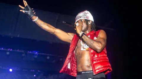 Getty Images Nigerian singer wearing a red puffer gilet over his bare torso on which he has many tattoos performs at a concert at Eko Energy City Gate, Lagos - 22 December 2024