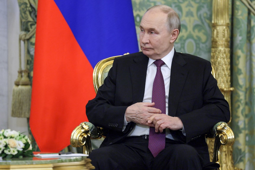 Vladimir Putin sitting in a golden chair in a ornate conference room.