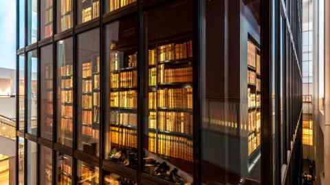 A glass-fronted tower of bookshelves in which can be glimpsed the reflections of people sitting reading at desks