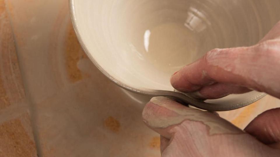 A pottery worker is working on a piece of clay. Fingers can be seen shaping the clay, which is light brown in colour.