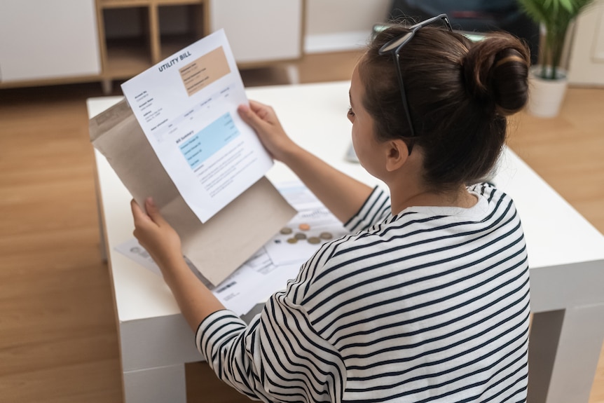 a woman is sitting at a table looking at a utility bill.