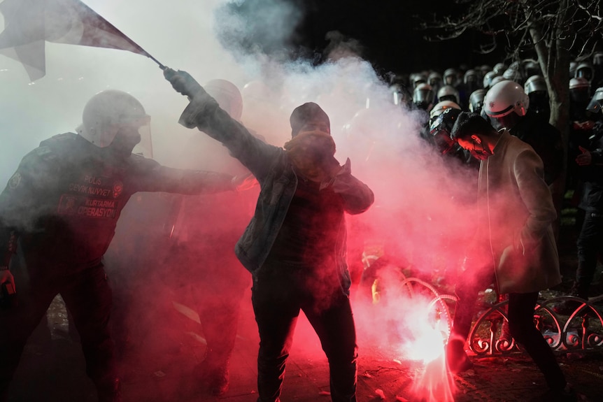 A person holding a flag is illuminated by red smoke