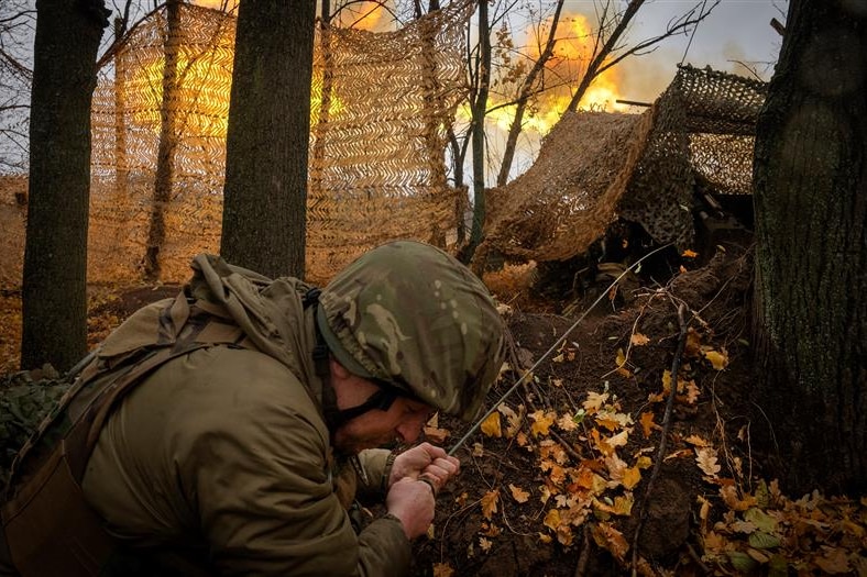 A Ukrainian soldier crouches down as he fries a gun toward enemy troops