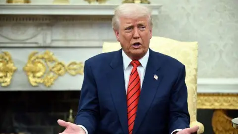 Getty Images President Trump wears a blue suit and red tie as he gestures while sat on a chair in the Oval Office at the White House