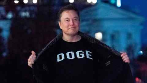 Elon Musk flashes his t-shirt that reads “DOGE” to the media as he walks on South Lawn of the White House